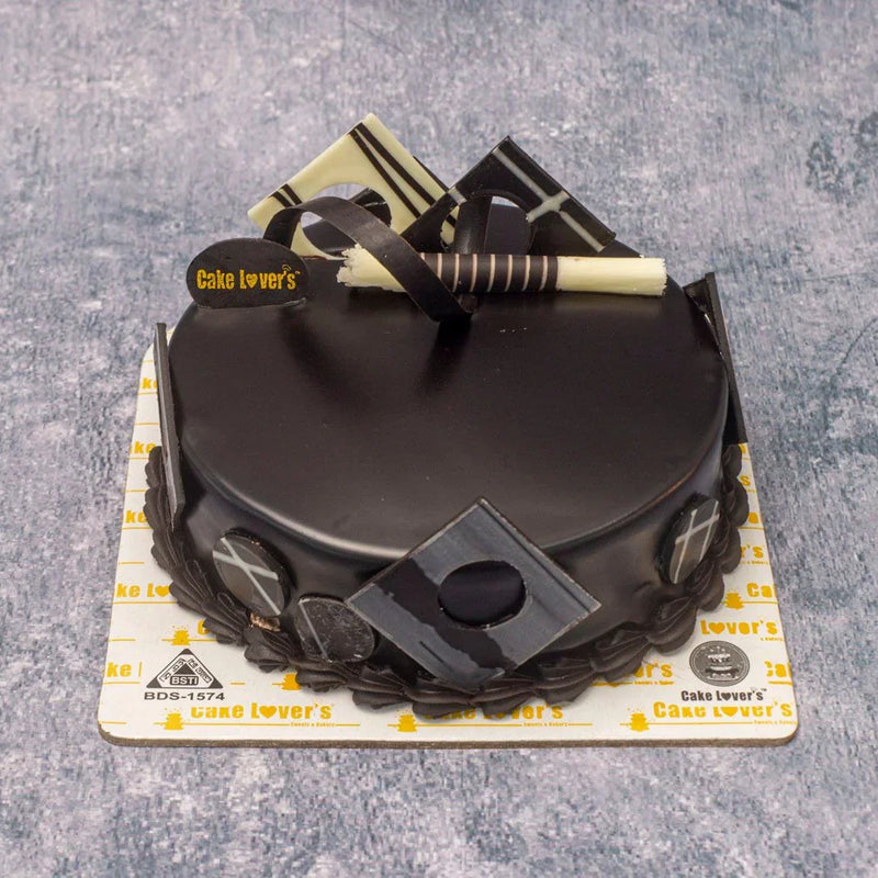 Black cake with decorative elements on a gray surface, branded 'Cake Lover's'.